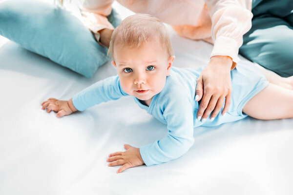 cropped shot of mother holding her child while he crawling on bed