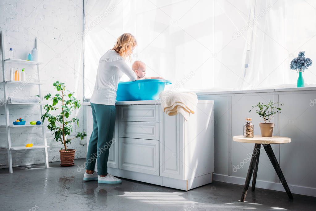 mother washing her little child in plastic baby bathtub at home