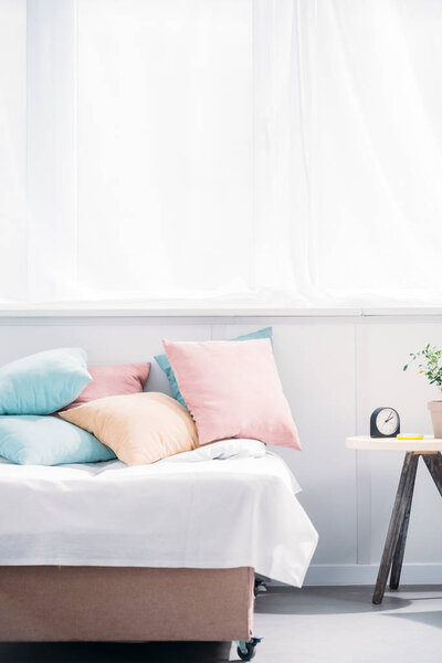 bed with lot of pillows in modern light room with alarm clock and plant of bedside table