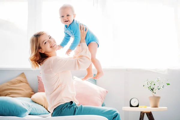 Vista Lateral Mãe Sorridente Levantando Criança Rindo Enquanto Sentado Cama — Fotografia de Stock