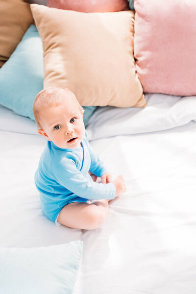 high angle view of adorable little baby sitting in bed and looking at camera