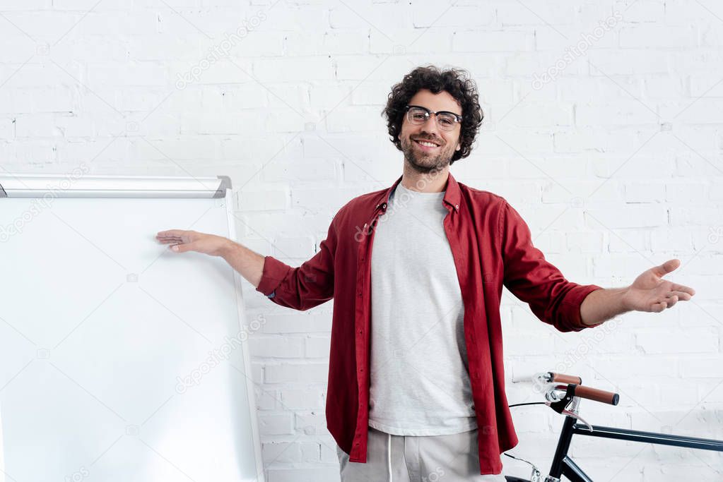 happy young man in eyeglasses pointing at whiteboard and smiling at camera 