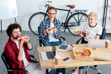 Genç meslektaşları işyerinde pizza yemek gülümseyen, yüksek açılı görünüş 