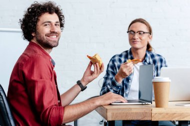 Pizza yemek ve dizüstü bilgisayarlar kullanma office gülümseyen genç erkekler