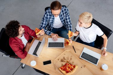 pizza yemek ve işyerinde dizüstü bilgisayarlar kullanarak genç meslektaşlarının havai görünümü