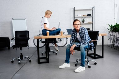 dizüstü bilgisayar ve ofis kamerada bakarak erkek meslektaşı kullanan genç kadın