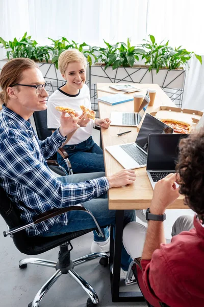 Smiling Young Colleagues Eating Pizza While Sitting Together Workplace — Free Stock Photo