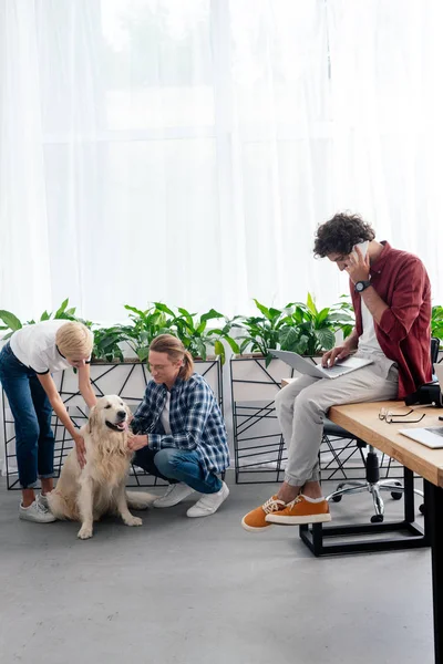 Joven Hablando Por Teléfono Inteligente Mientras Colegas Acariciando Perro Oficina —  Fotos de Stock