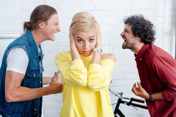 Young Woman Closing Ears Looking Camera While Male Colleagues Yelling — Stock Photo, Image