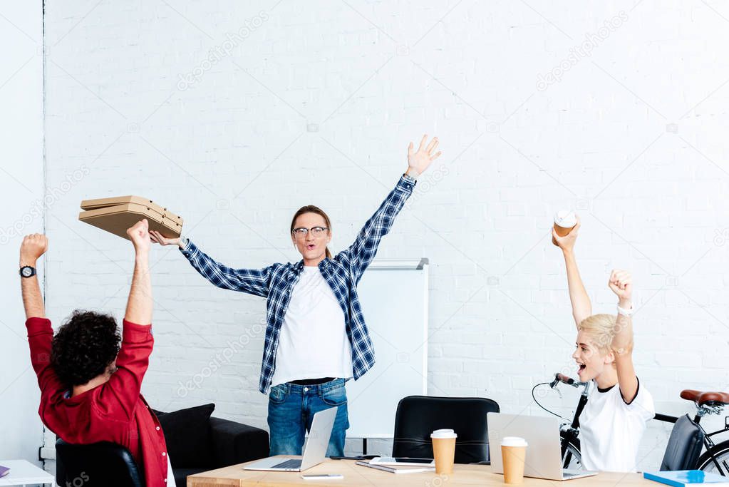 excited young start up team raising hands and looking at pizza boxes in office