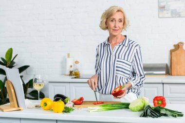 güzel kadın kıdemli mutfak ahşap tahta üzerinde kırmızı dolmalık biber kesme 