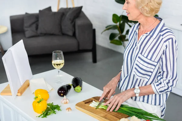 Atractiva Mujer Pelo Gris Cortando Cebolla Verde Cocina Mirando Libro — Foto de stock gratis