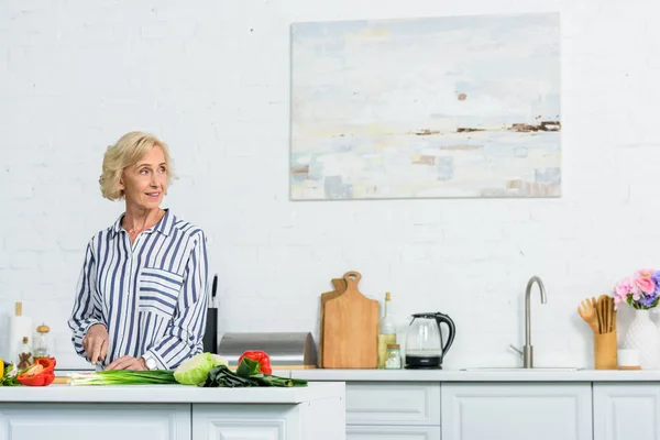 Atractiva Mujer Pelo Gris Cortando Verduras Cocina Mirando Hacia Otro — Foto de Stock