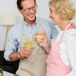 Glimlachend senior paar rammelende met glazen wijn tijdens het koken in de keuken