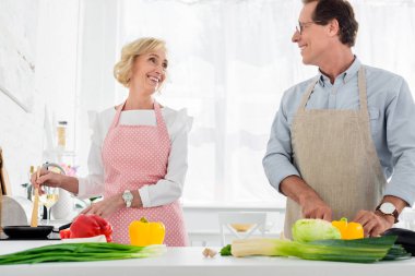 happy senior couple cooking together at kitchen and looking at each other clipart