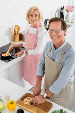 high angle view of senior couple cooking together at kitchen and looking at camera clipart