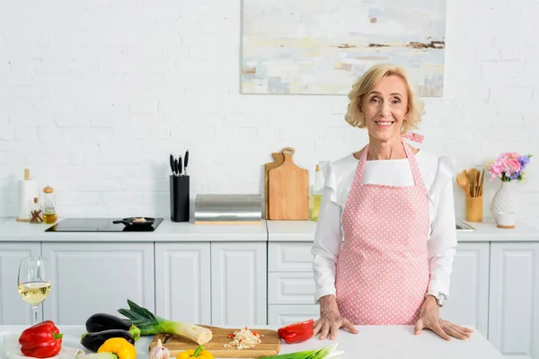 Lächelnde Attraktive Seniorin Steht Küchentisch Und Blickt Die Kamera — Stockfoto