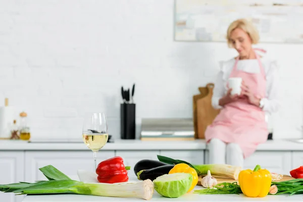 Красивая Пожилая Женщина Сидит Кухонном Столе Чашкой Чая Овощами Переднем — стоковое фото