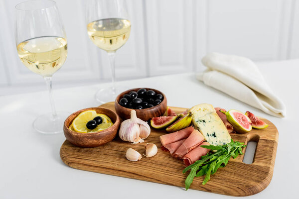 close-up view of delicious snacks on wooden board and glasses of wine on table    
