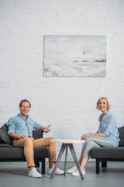 birlikte evde otururken kameraya gülümseyen mutlu yaşlı çift 