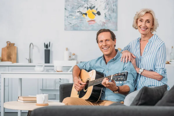 Feliz Pareja Ancianos Sonriendo Cámara Mientras Hombre Tocando Guitarra Casa — Foto de Stock