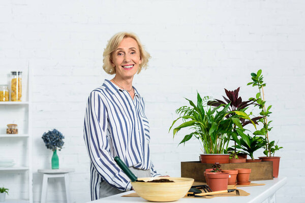 happy senior woman smiling at camera while cultivating potted plants at home