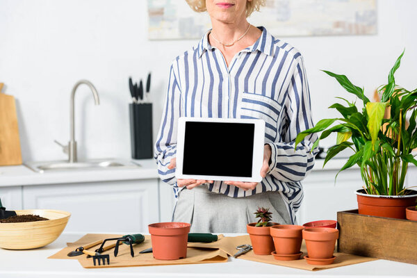 cropped shot of senior woman holding digital tablet with blank screen while cultivating plants at home