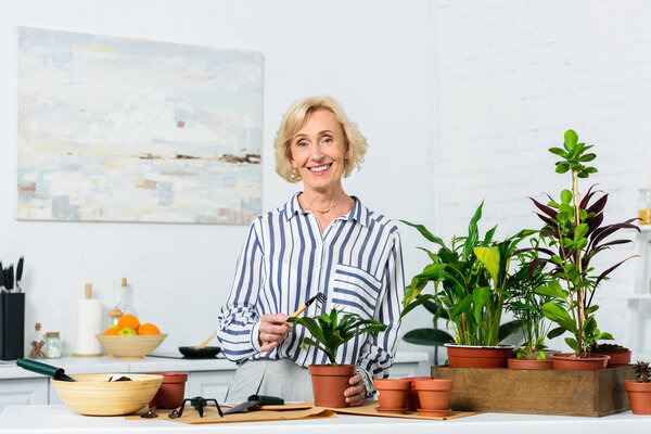 happy senior woman smiling at camera while cultivating potted plants at home 