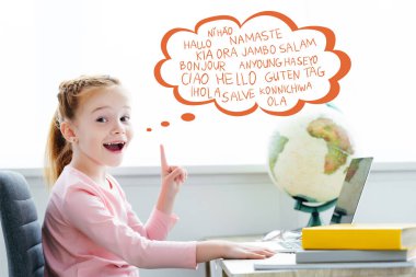 redhead schoolchild studying with books and laptop and pointing up on words on different languages in speech bubble  clipart