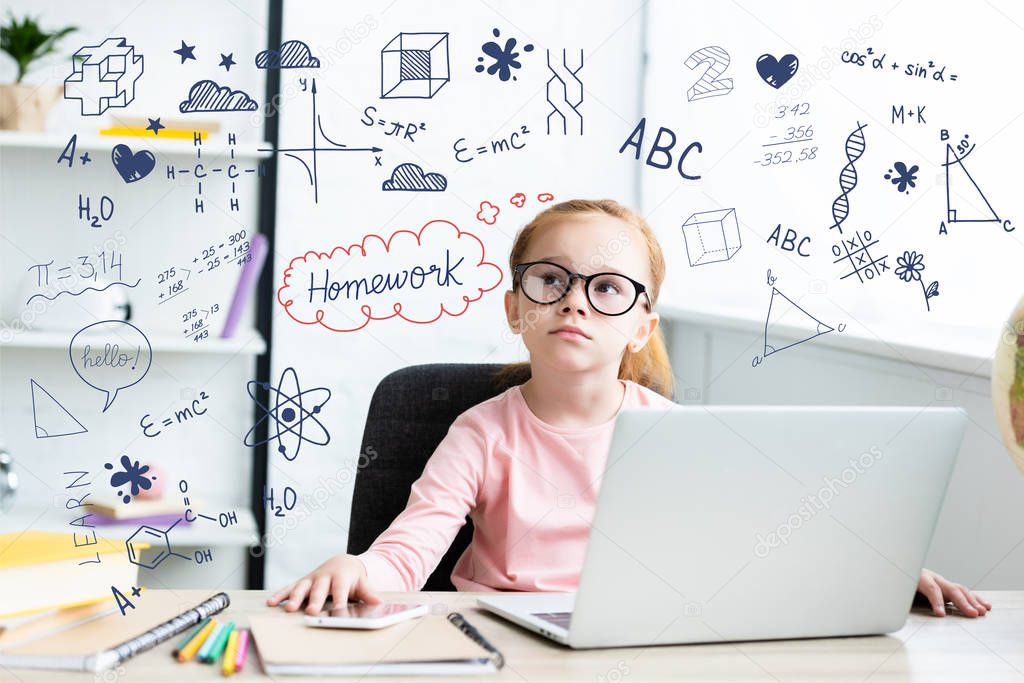 Thoughtful little schoolchild in eyeglasses looking up while sitting at desk and using laptop with learning icons