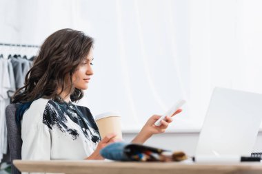 kahve fincan masada dizüstü bilgisayar ile smartphone kullanarak ile kadın moda tasarımcısı gülümseyen