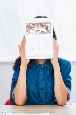 Genç kadın tarafından dijital tablet ekranında oturaklı Web sitesi ile yüz kapsayan 