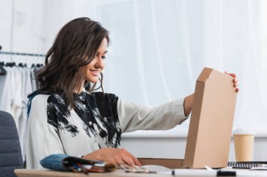 kadın tasarımcı pizza kutusu masada kağıt bardak kahve ile açılış gülümseyen 