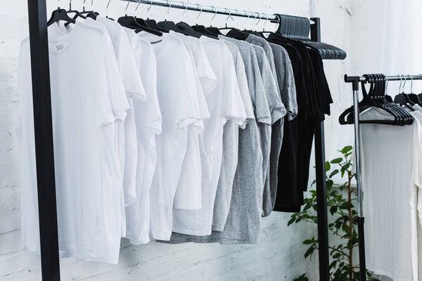 selective focus of white, black and grey empty t-shirts on hangers in clothing design studio 