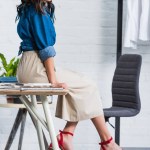Atraktivní ženské módní návrhář sedí na stole v ateliéru design oděvu