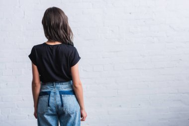 rear view of young woman in empty black t-shirt in front of brick wall  clipart