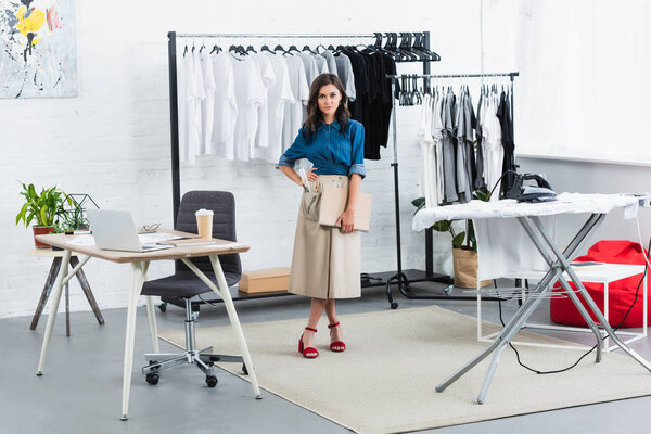 дизайнер женской одежды, стоящая с учебником в студии дизайна одежды
