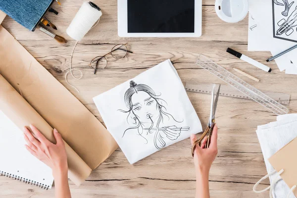 stock image cropped image of female fashion designer with scissors sitting at table with paintings and digital tablet 