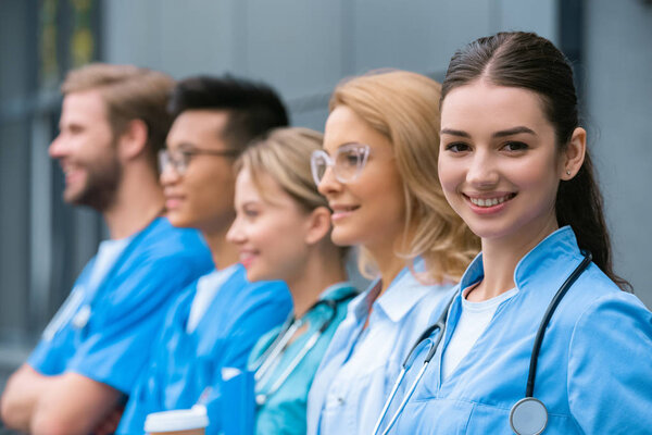 teacher and happy multicultural students standing in row near medical university