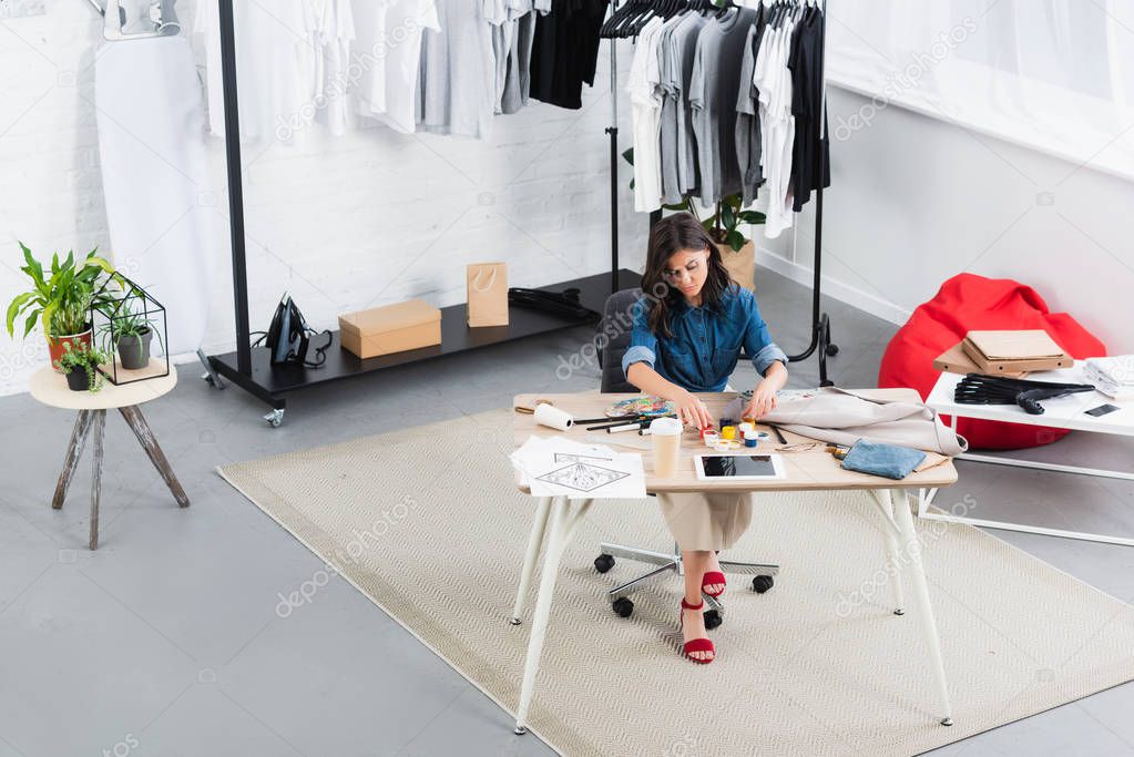high angle view of female fashion designer painting on jacket at working table in clothing design studio