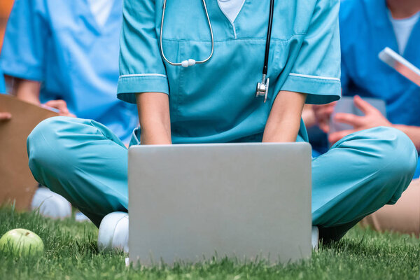 cropped image of medical student studying with laptop on green grass