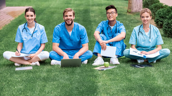 multicultural medical students sitting on grass and looking at camera