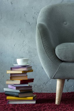 stack of books and cup of coffee on burgundy carpet near grey armchair in office clipart