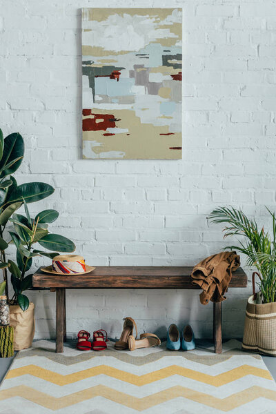 different shoes under wooden bench in corridor at home, painting on wall
