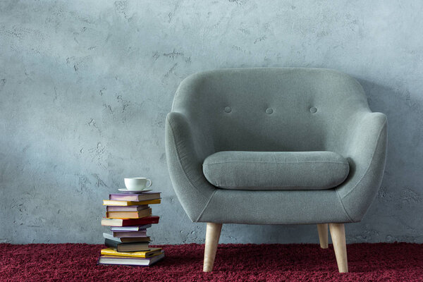 stack of books and cup of coffee near grey armchair in office
