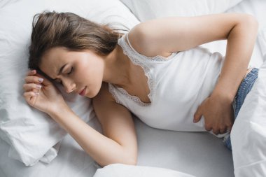 high angle view of young woman suffering from stomach ache in bed clipart