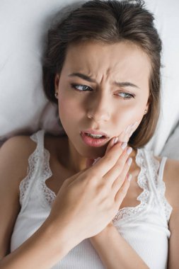 attractive young woman suffering from toothache while lying in bed   clipart