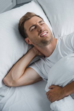 yatakta yatan ve boyun ağrısı muzdarip bir genç adam 