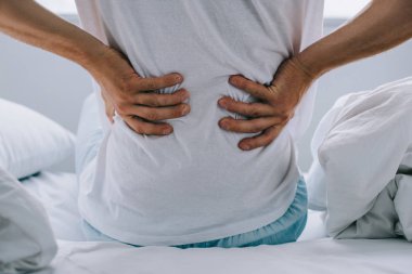 cropped shot of man sitting on bed and suffering from back pain clipart