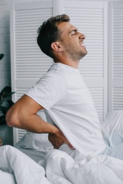 Genç adam yatakta otururken sırt ağrısı muzdarip pijama yan görünüm   